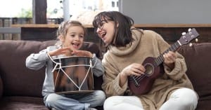 Little girl playing drum with her teacher who is playing ukulele