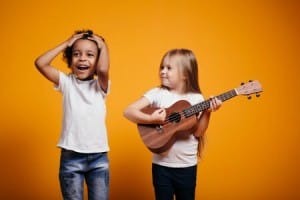 Two toddlers playing ukulele, happily smiling, having fun