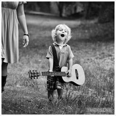 Toddlers holding an small acoustic guitar, so glad singing. Black and white picture.