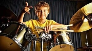 Happy boy, playing drums. Wearing yellow T-shirt.