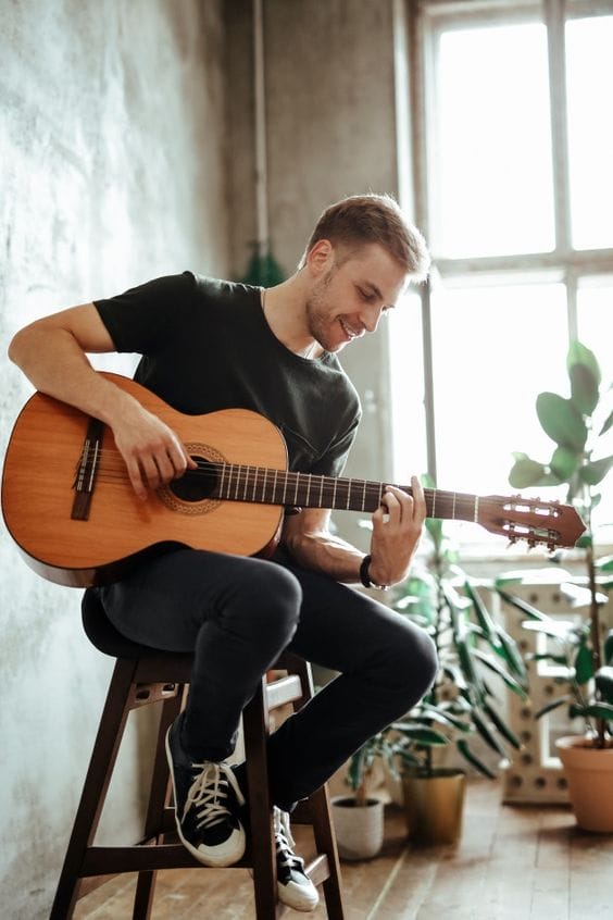 Young man joyfully playing an acoustic guitar, sitting on a stool.