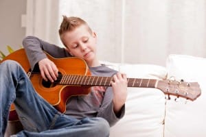 Pre-adolescent boy, so glad, playing the guitar. Wearing gray sweatshirt.